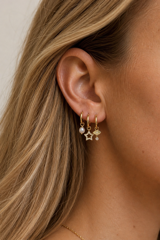 Close-up of an ear wearing gold earrings with pearls and stars, against a neutral background.