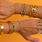 Gold jewelry including bracelets and rings on a person's wrist against an orange background