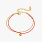 Gold bracelet with a heart charm on a red cord against a white background