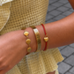 Close-up of a wrist wearing gold and red bracelets with a textured beige outfit.