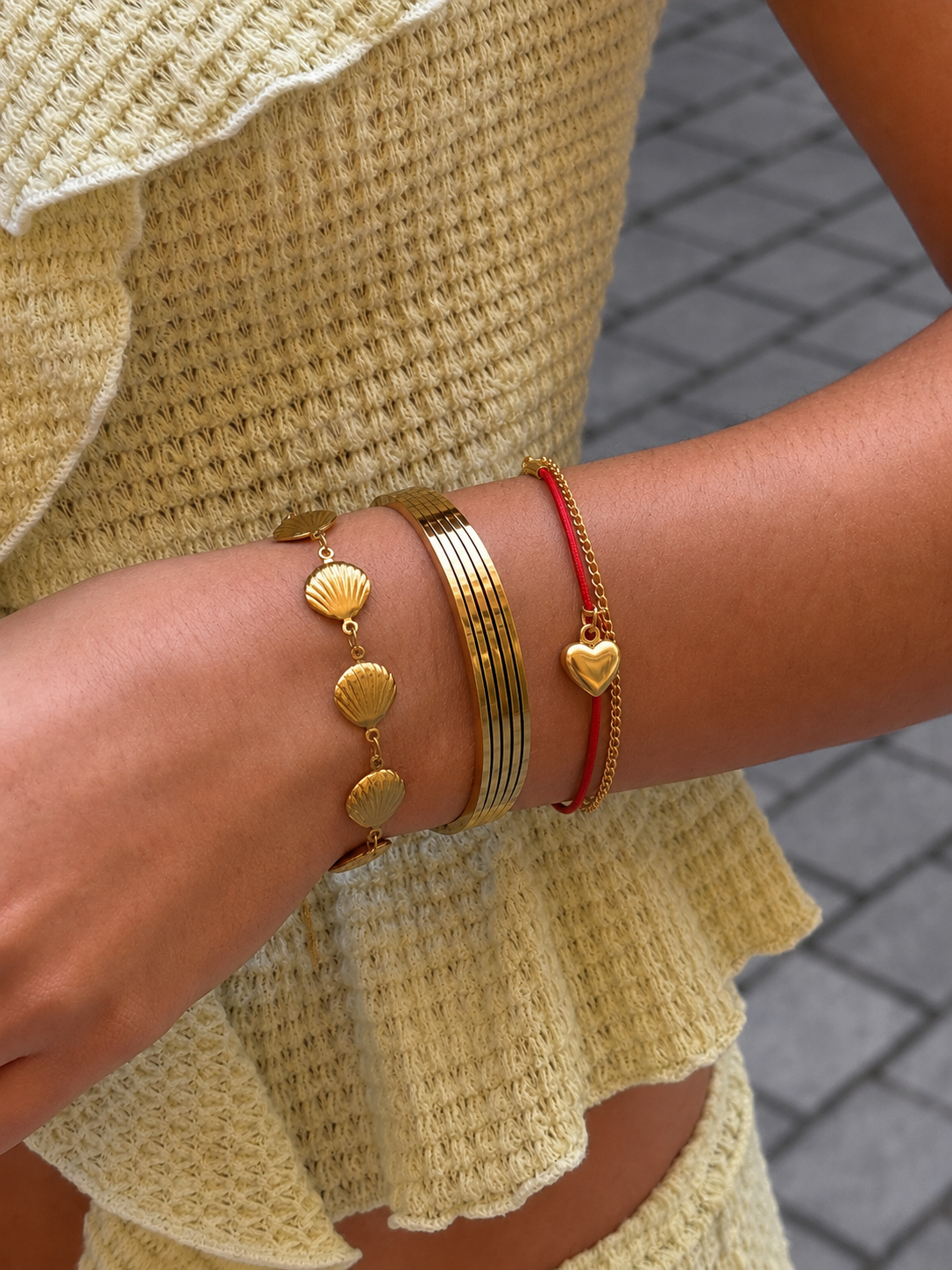 Close-up of a wrist wearing gold and red bracelets with a textured beige outfit.