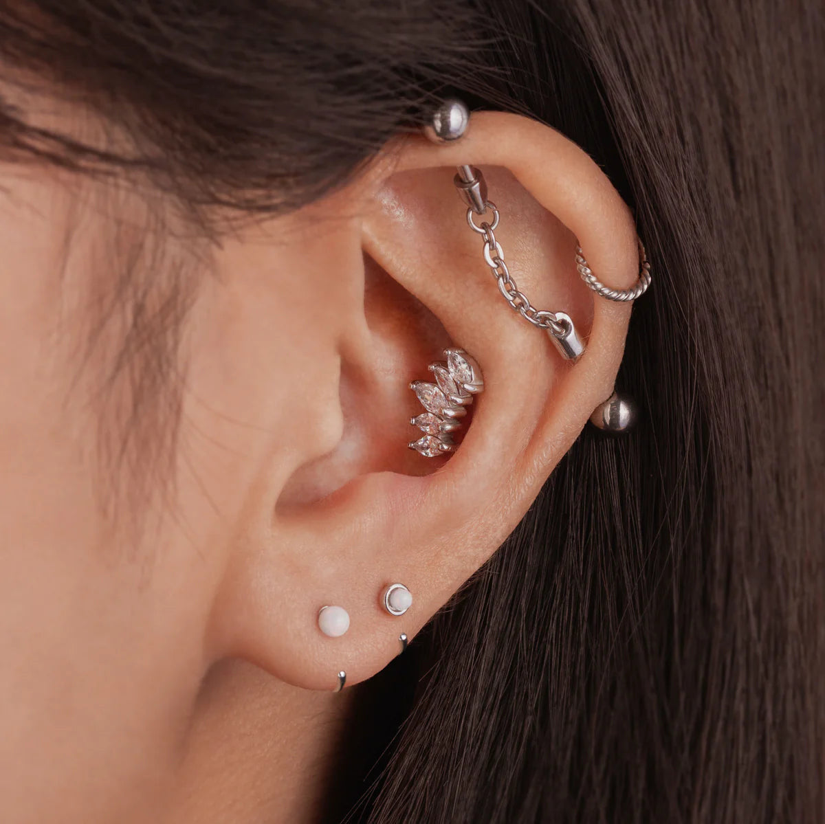 A pair of gold-colored hoop earrings with white opal stones set in them in ear