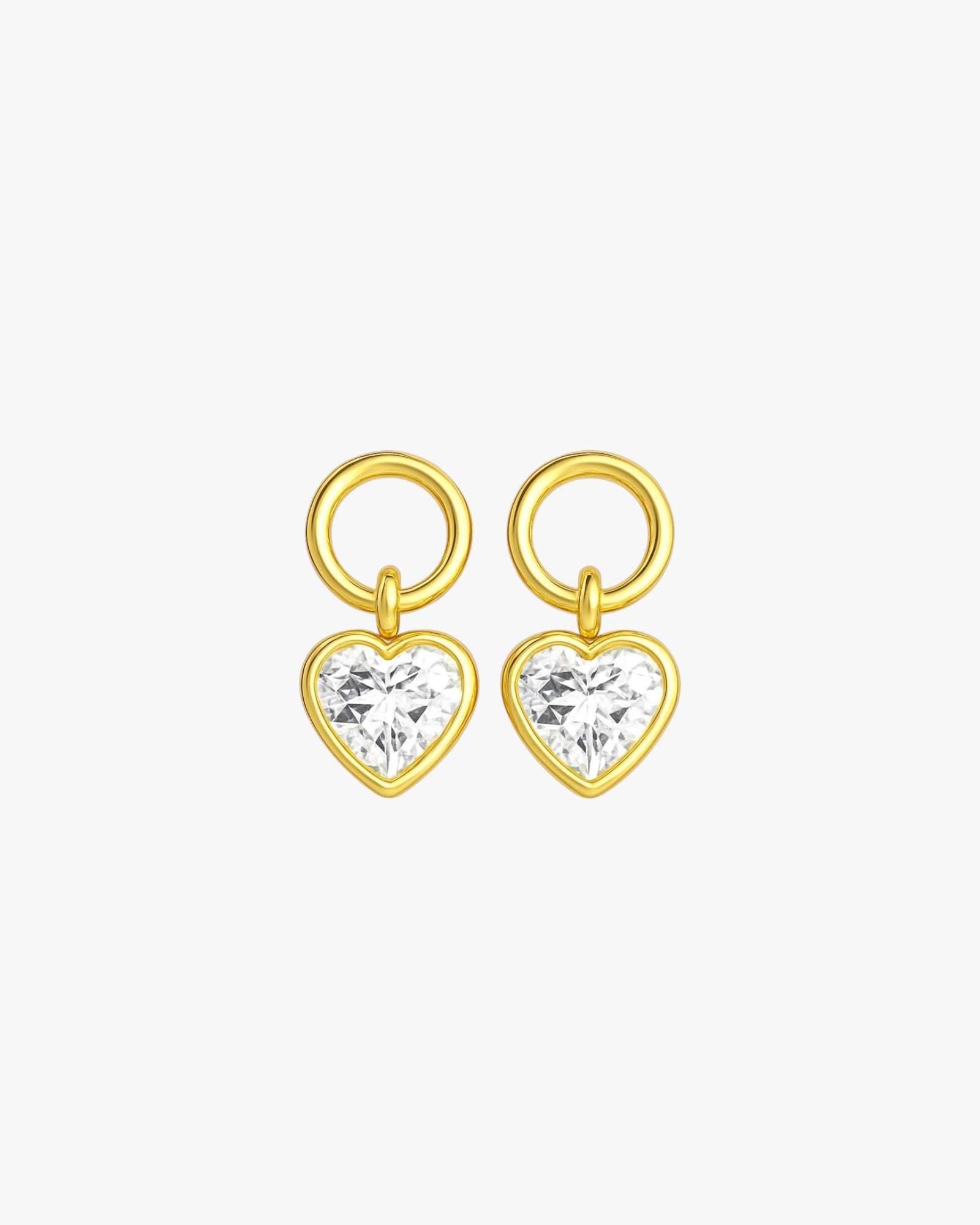 Gold heart-shaped earrings with clear gemstones on a light gray background