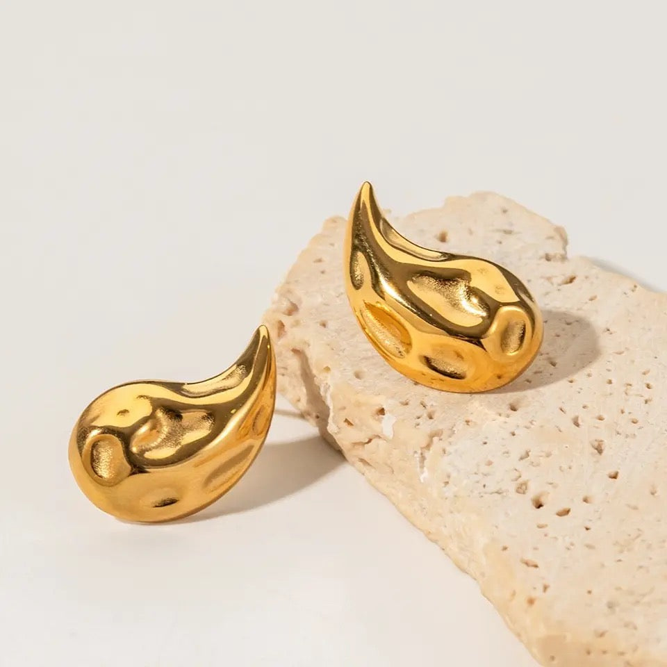 "Image: Gold drop earrings elegantly displayed on a stone surface."