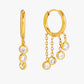 Gold hoop earrings with dangling gemstones on a white background